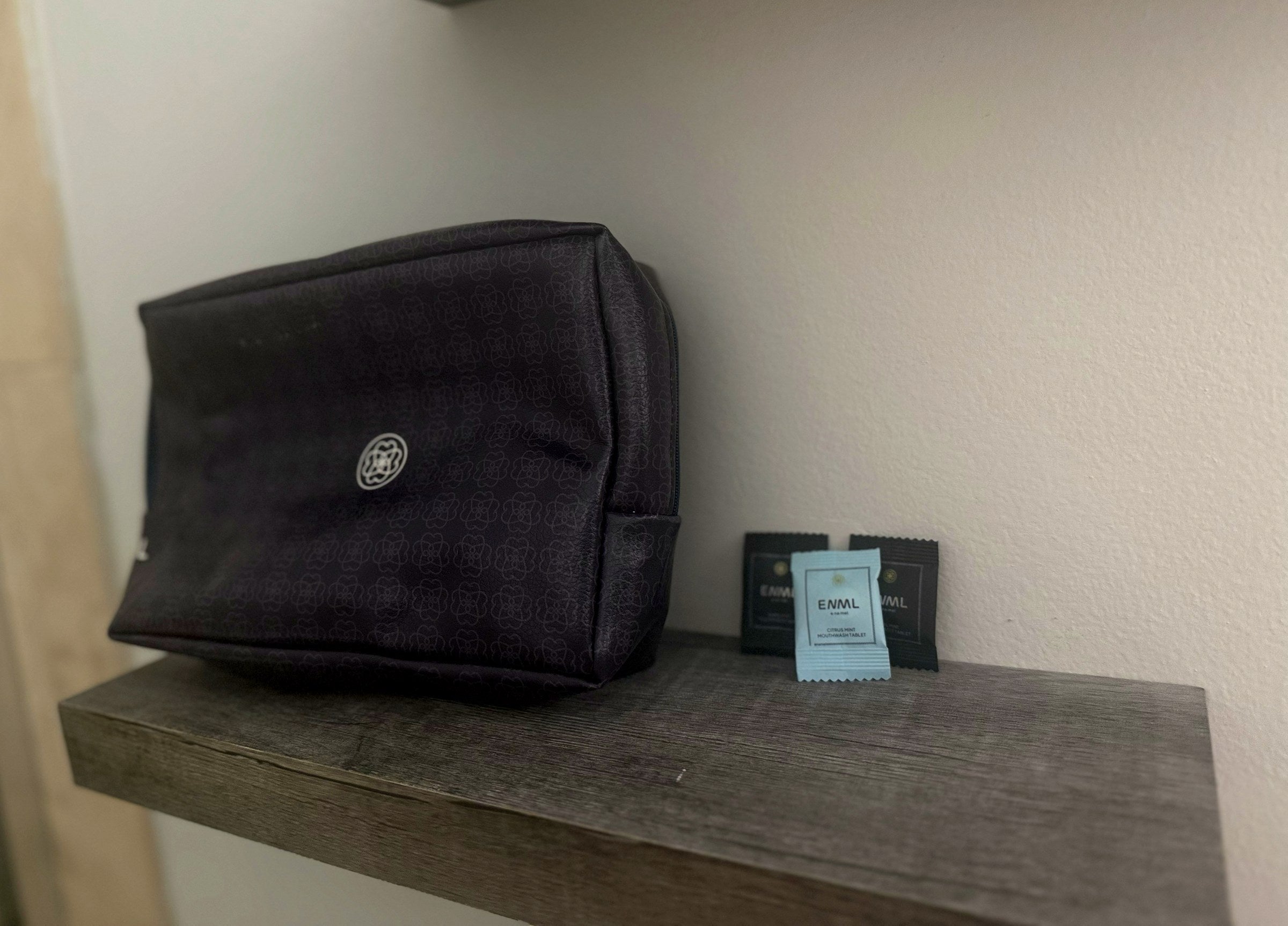 ENML single-use toothpaste and mouthwash tablet packets beside a travel bag on a guest bathroom shelf